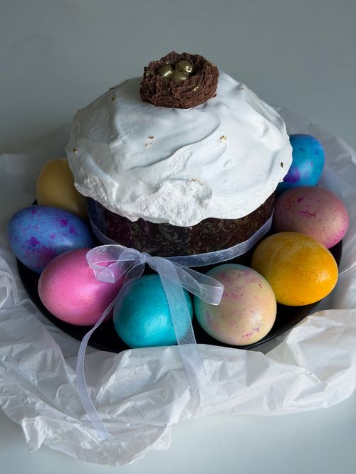 Free A festive Easter cake topped with icing and surrounded by colorful, decorated eggs on a table. Stock Photo