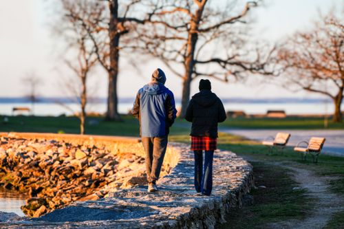 Free A couple strolls along a rocky path in a serene autumn park by a lake. Stock Photo
