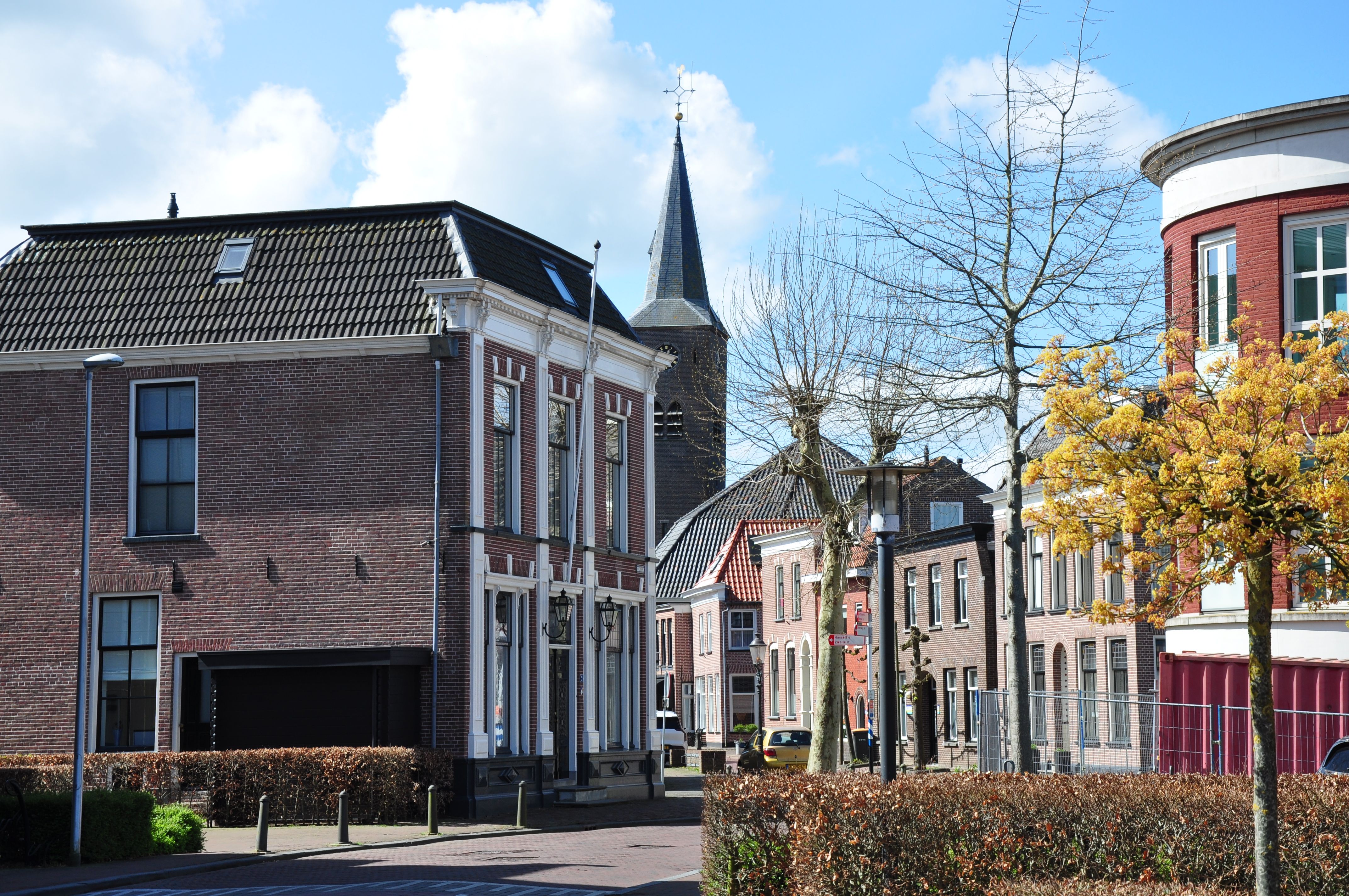 Picturesque European street view featuring historical brick buildings and a church tower under a blue sky.