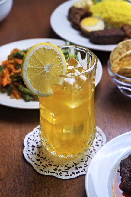 A tall glass of John Daly drink with amber iced tea and pale lemonade layered over ice, garnished with a lemon wheel.