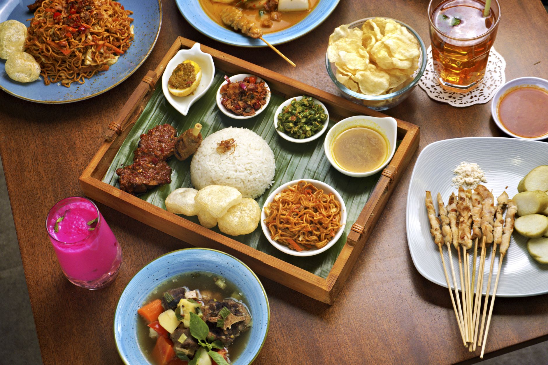 Indonesian meal featuring sate, nasi campur, and various side dishes on a wooden table.