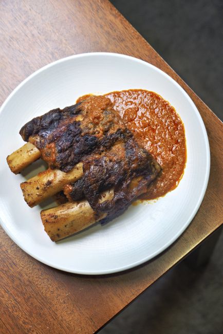 A baking dish of glazed country style ribs with charred, caramelized edges and barbecue sauce pooling around them, garnished with chopped parsley.