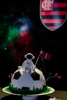 A creative soccer-themed cake featuring an astronaut topper and a team flag, set against a cosmic background.