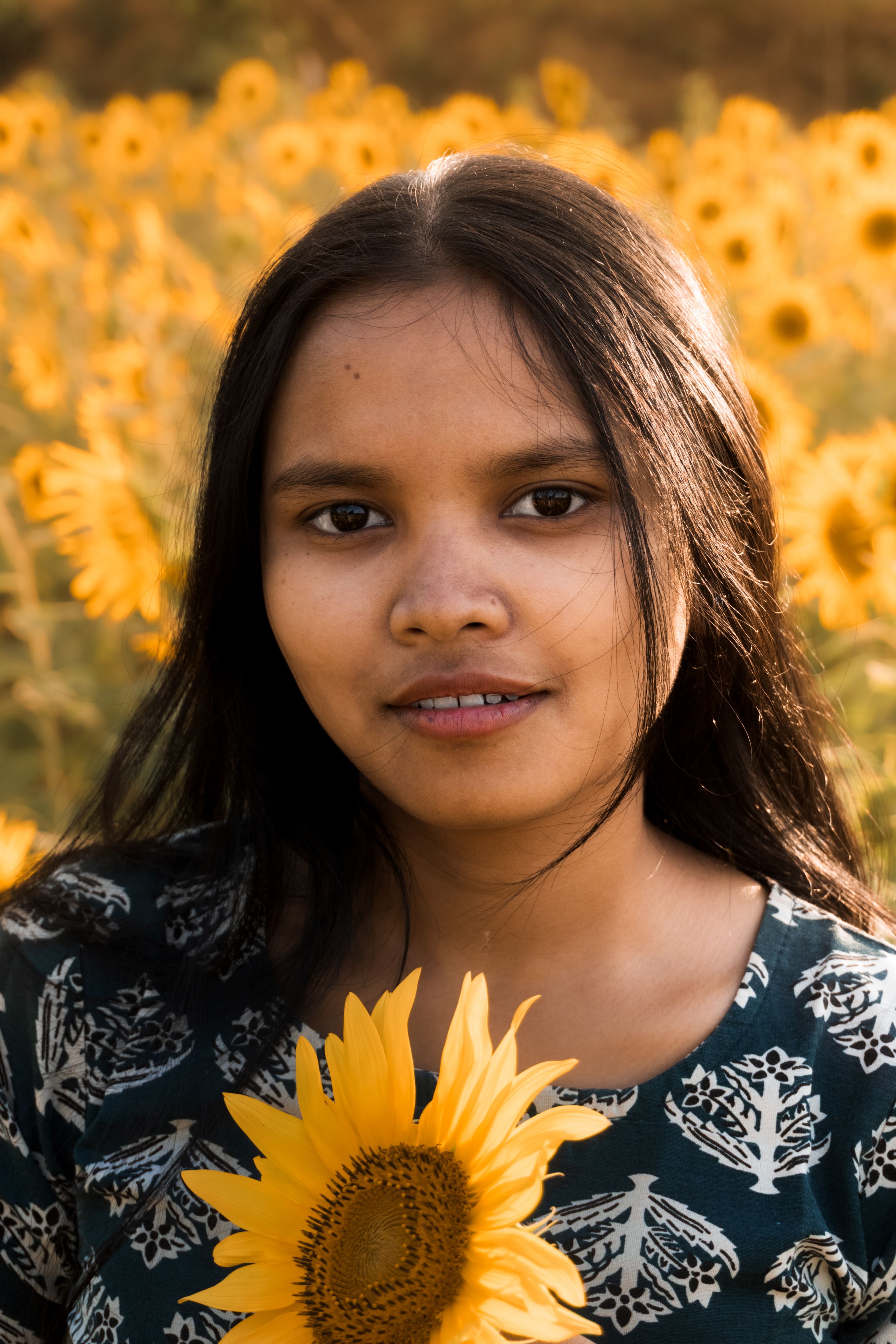 A young woman holding a sunflower, surrounded by a lush sunflower field under daylight.