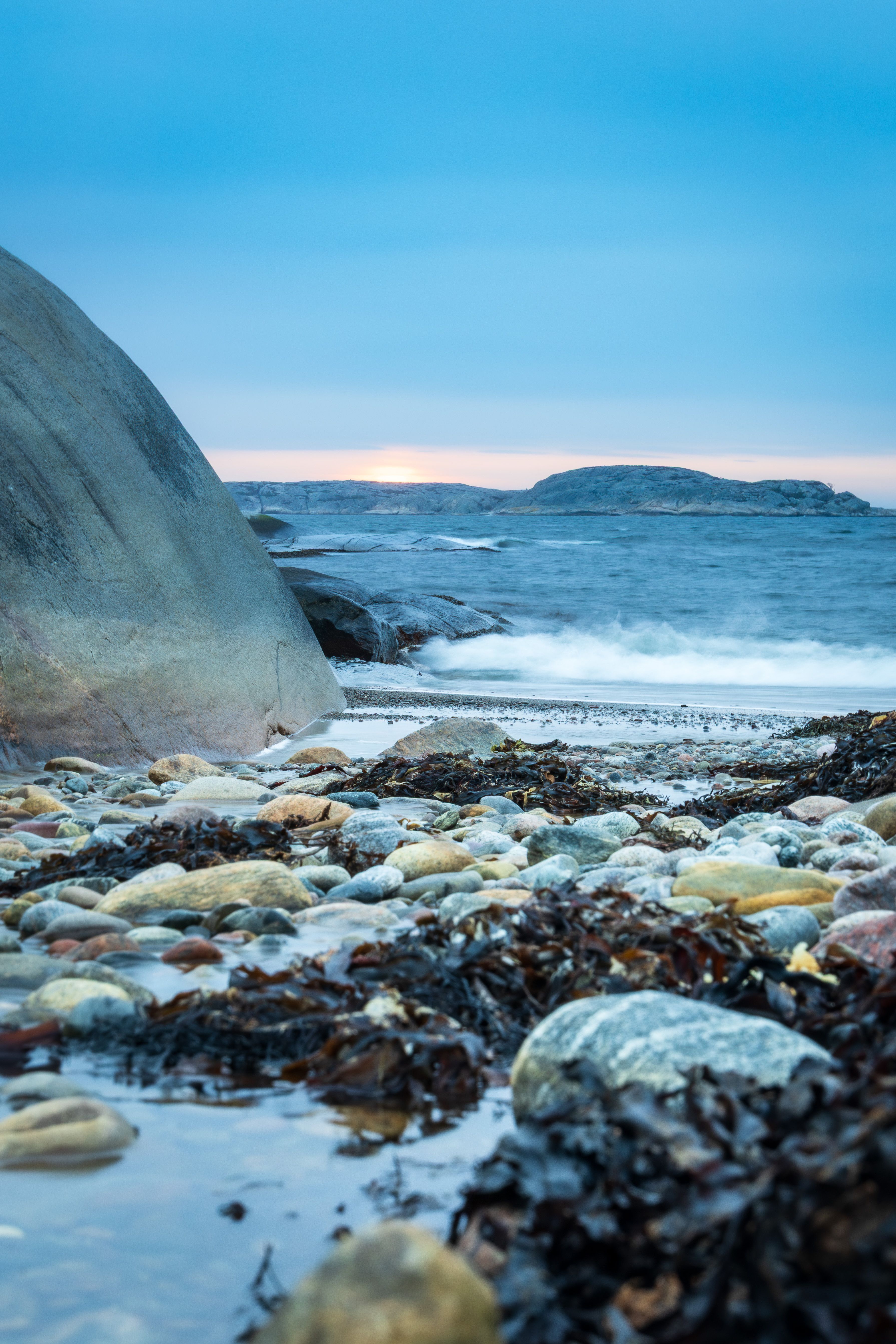 Gratis Fredfyldt stenstrand i Gullbringa, Sverige, med en dramatisk solnedgang og beroligende havbølger. Lagerfoto