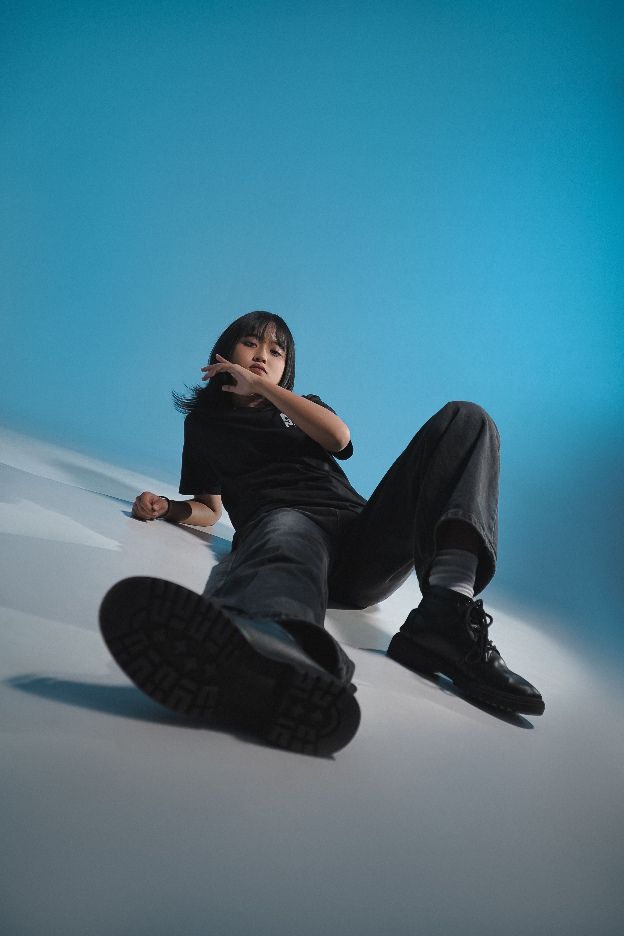 Stylish young adult posing casually indoors against a gradient blue backdrop.