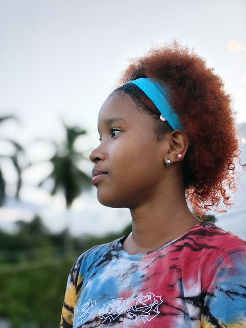 Free Profile of a young woman wearing a blue headband with colorful hair, set against a tropical outdoor background. Stock Photo
