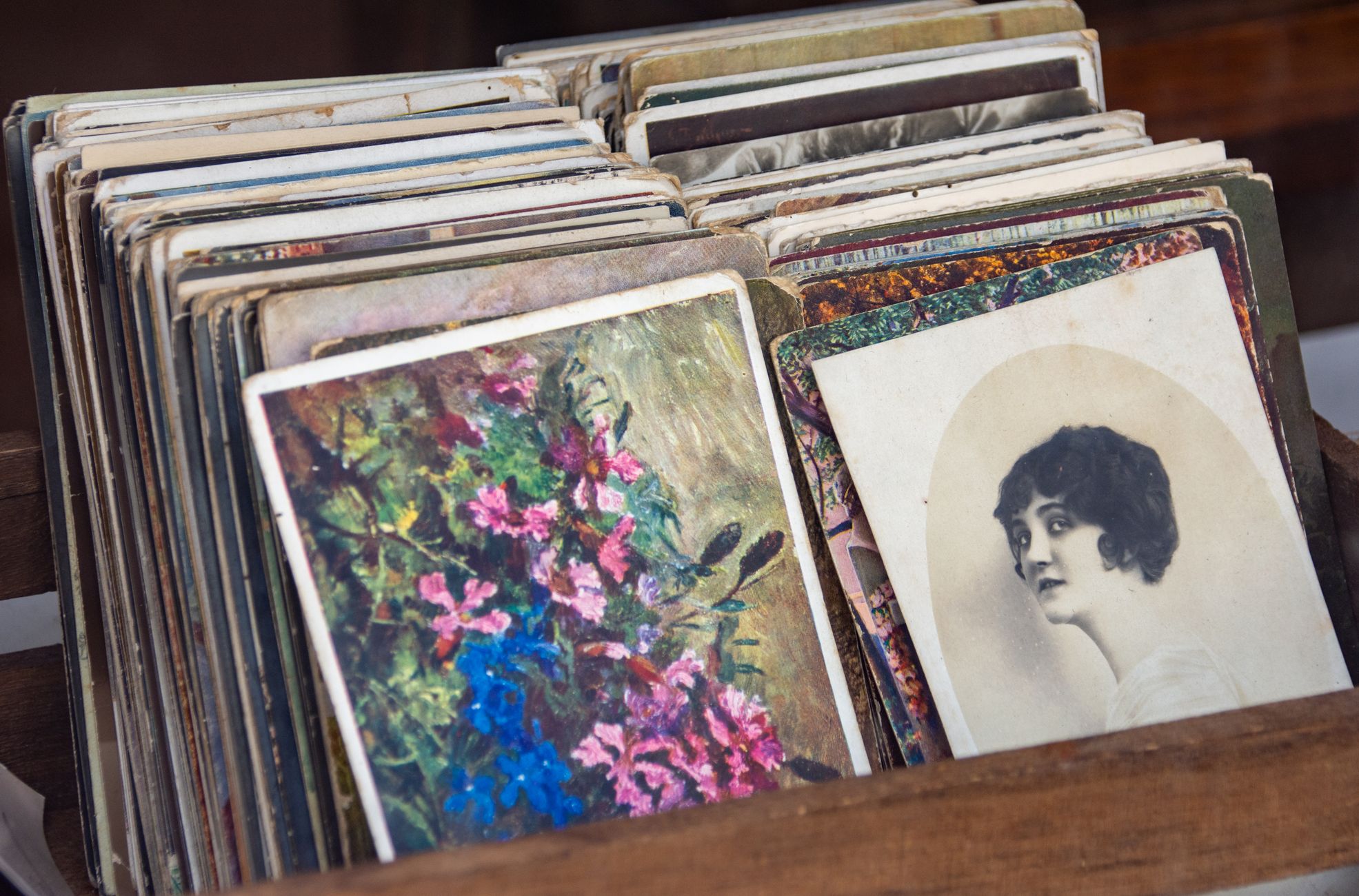 Collection of vintage postcards in a wooden box featuring floral art and a sepia portrait.