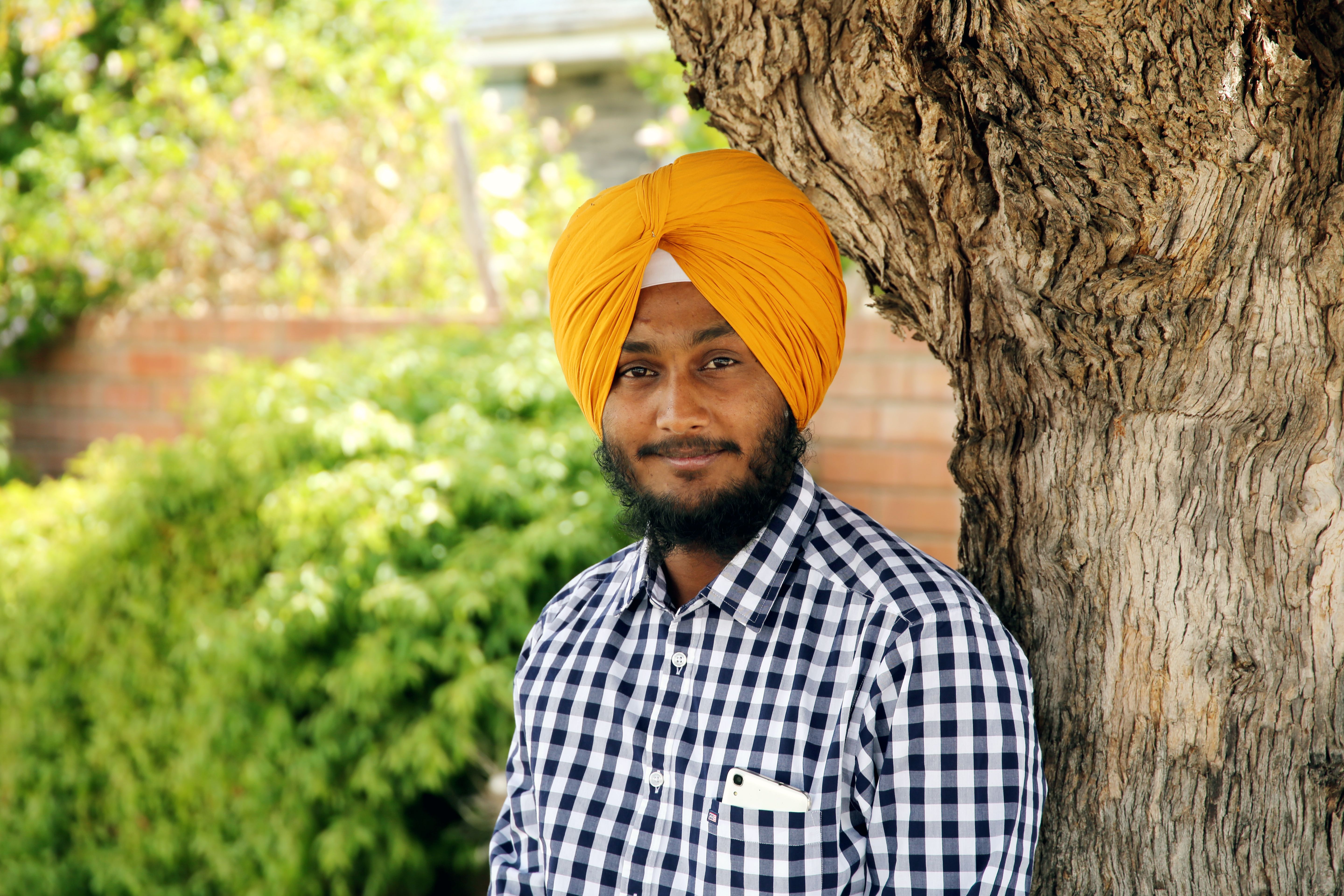 Smiling man with a yellow turban stands under a tree in a garden setting.