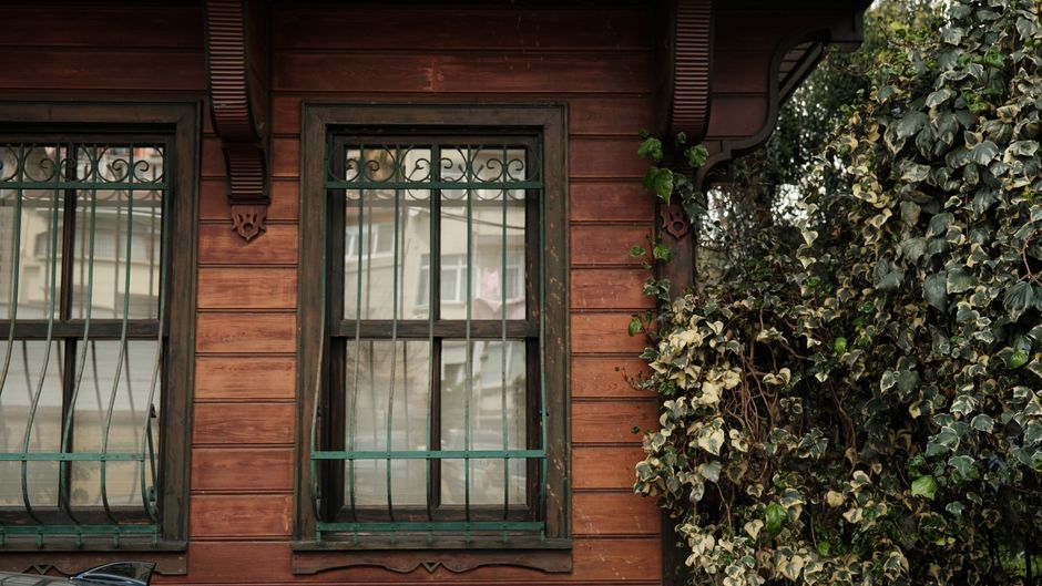 A rustic wooden house facade with iron-barred windows surrounded by ivy.