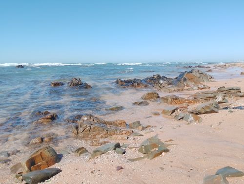 Free Scenic view of a rocky beach with clear blue waters under a bright sky. Stock Photo