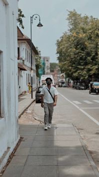 Man walking casually on a tree-lined street in Thiruvananthapuram, India, on a sunny day.