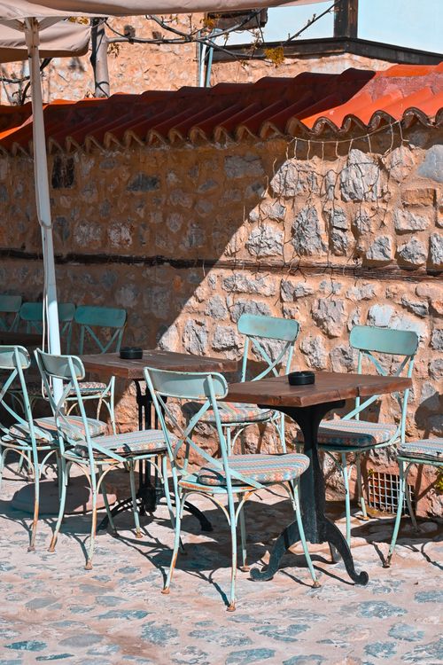 Free Sunny outdoor cafe setting with vintage teal chairs and stone wall backdrop. Stock Photo
