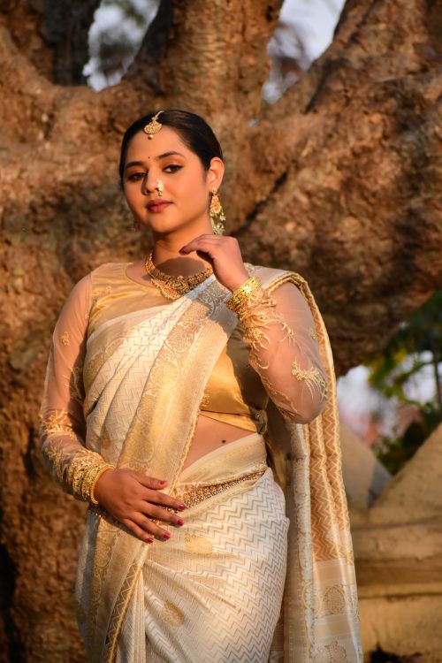 Free A woman in a traditional white and gold saree poses gracefully outdoors. Stock Photo