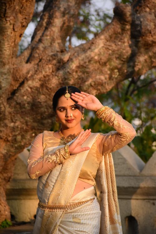Free Traditional Indian dancer gracefully posing in a sari outdoors with a serene tree backdrop. Stock Photo