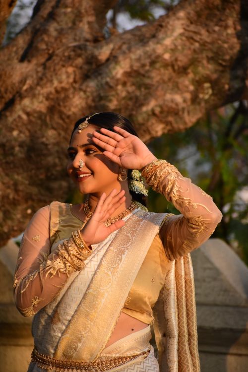 Free Smiling woman in a golden sari posing outdoors with a scenic backdrop. Stock Photo