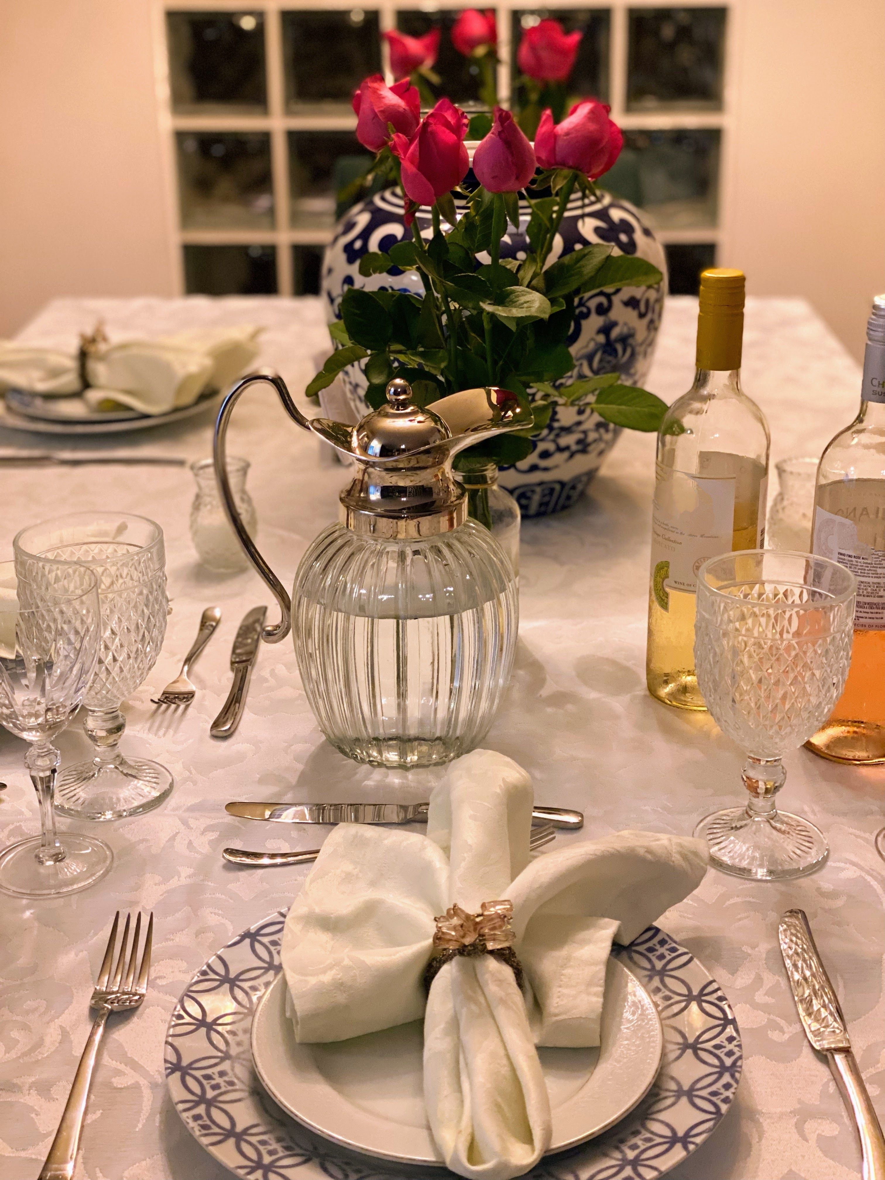 Mesa de jantar lindamente posta com rosas, cristais, vinho e talheres elegantes.