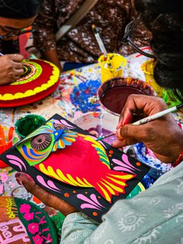 Vibrant artisan painting with colorful patterns in a traditional craft setting.