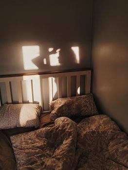 Soft morning sunlight casts shadows over a cozy unmade bed with patterned bedding.