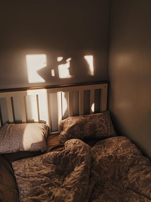 Soft morning sunlight casts shadows over a cozy unmade bed with patterned bedding.