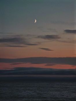 A serene seascape with a crescent moon and colorful twilight sky.