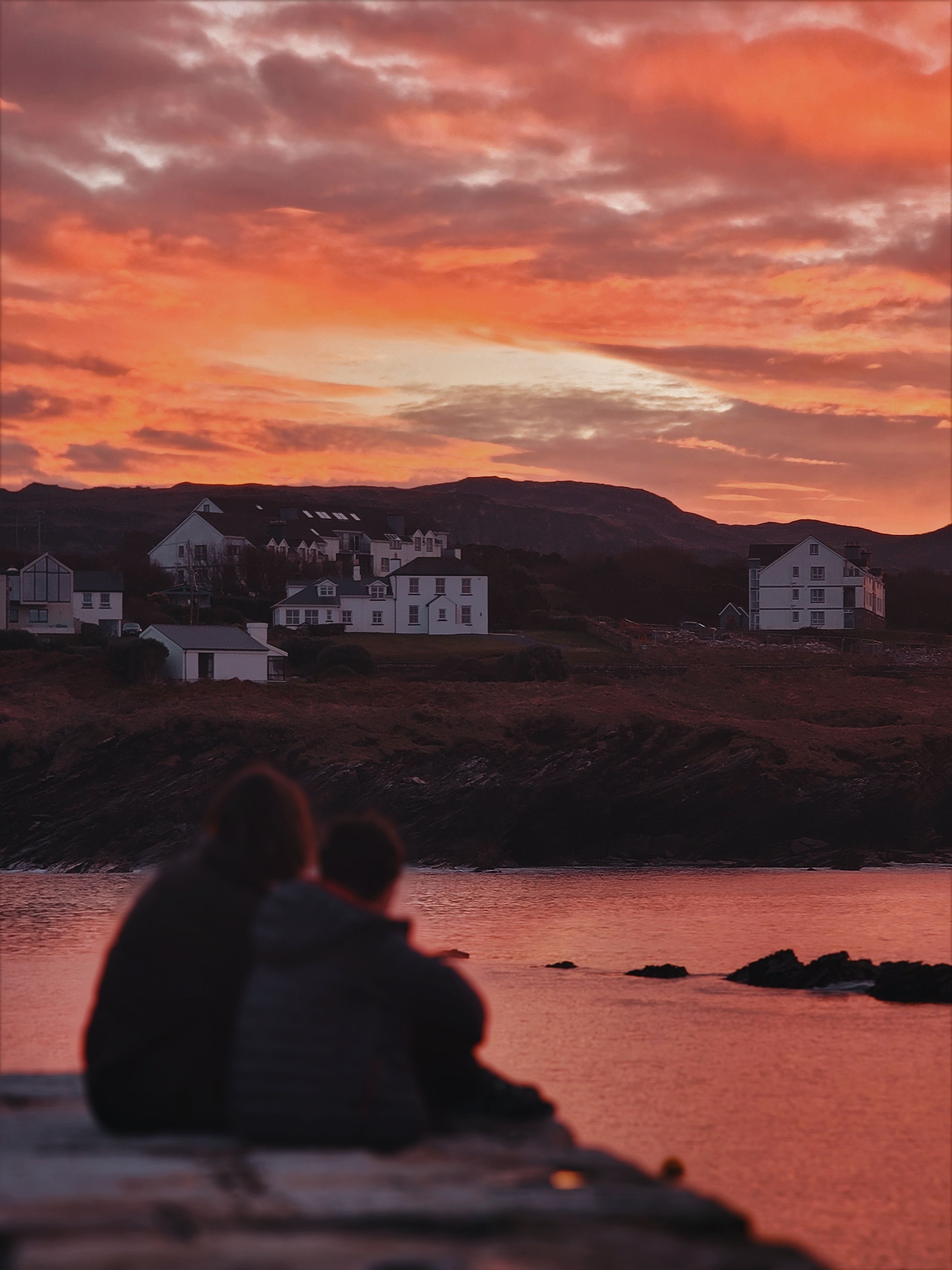 Silhouetted couple enjoying a serene sunset over a peaceful coastal village with vibrant skies.