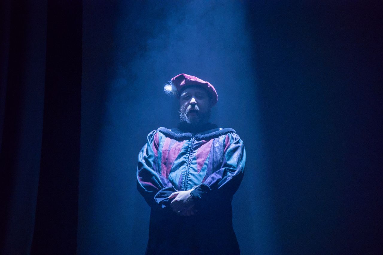 actor in period costume on stage under dramatic spotlight with theatri
