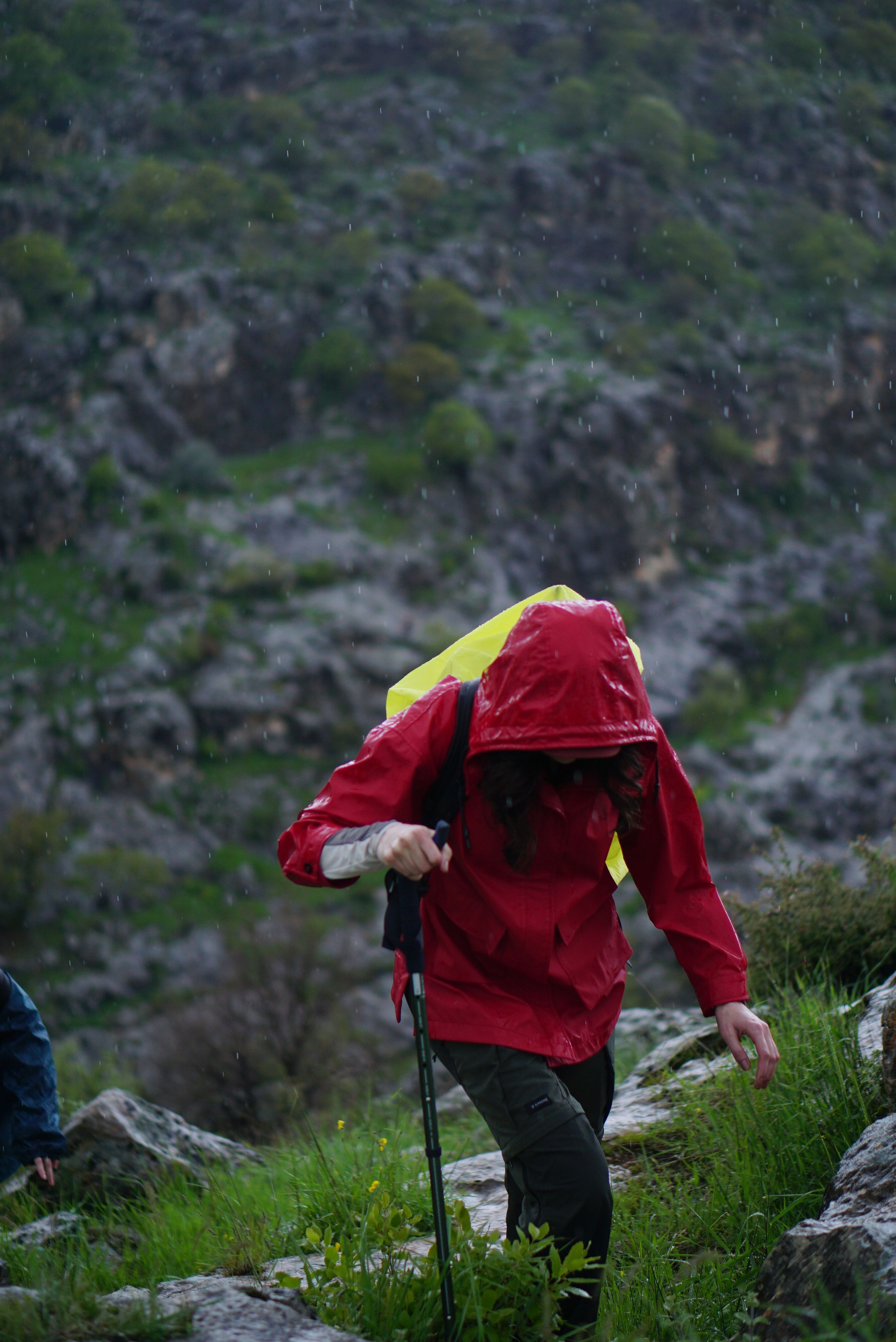 Hiker in hardshell rain jacket on rocky mountain trail during storm