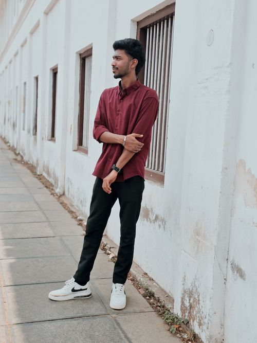 Free Young man in casual attire, standing by a building wall on a sidewalk. Stock Photo