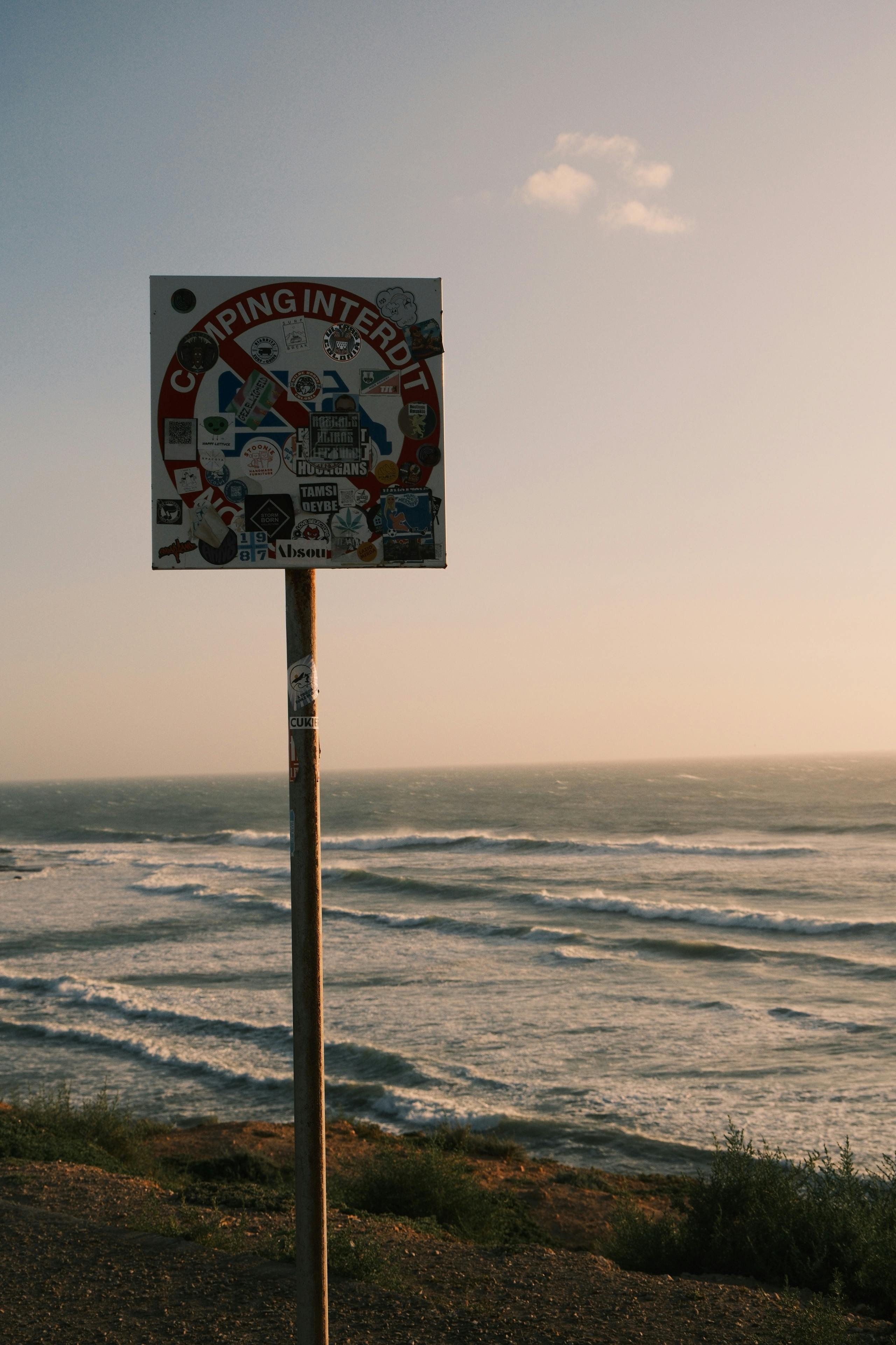 No camping sign against a picturesque coastal backdrop at sunset, reflecting travel restrictions.
