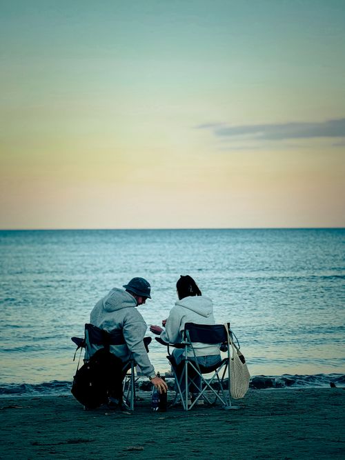 Free A serene twilight scene with a couple enjoying the ocean view from camping chairs on the beach. Stock Photo