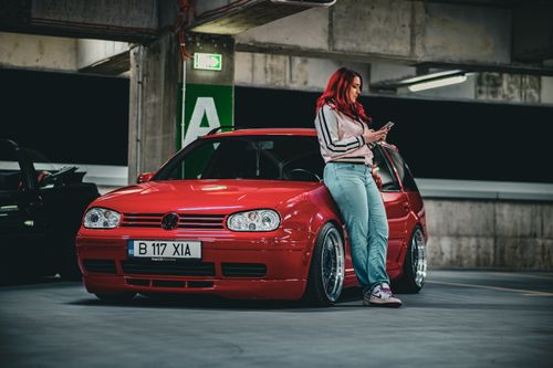 Free Woman with red hair leaning on a red car in a parking garage, checking phone. Stock Photo
