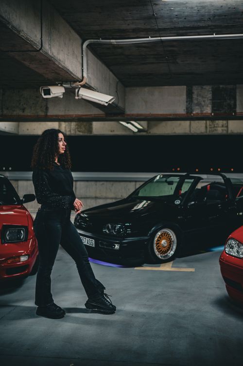 Free A woman walks through a moody underground parking garage with a focus on vintage cars and edgy fashion. Stock Photo