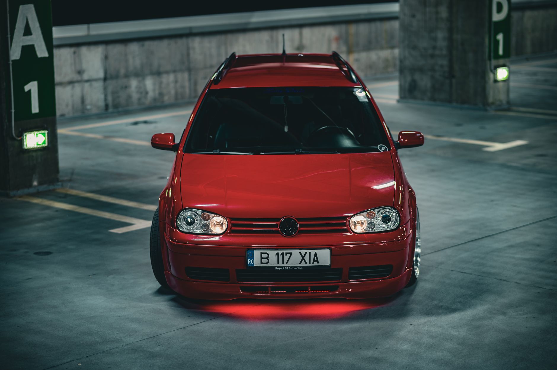 A striking red car shown parked in a dimly lit underground garage, with a focus on its vibrant color and sleek design.