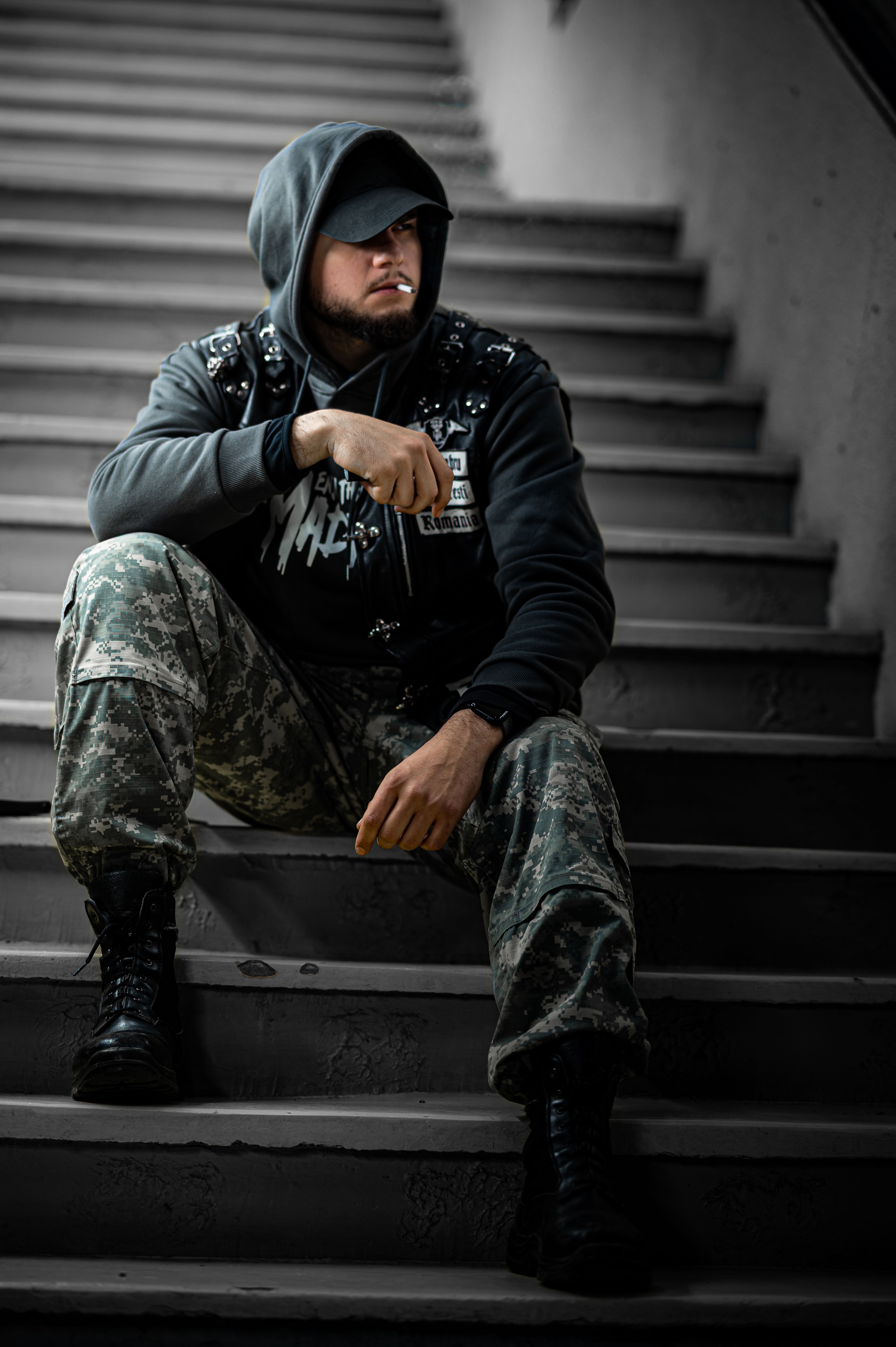 A man in a hooded sweatshirt and camouflage pants sits thoughtfully on a stairwell.