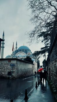 Two people walk with umbrellas near a mosque in Istanbul, Turkey on a rainy day.