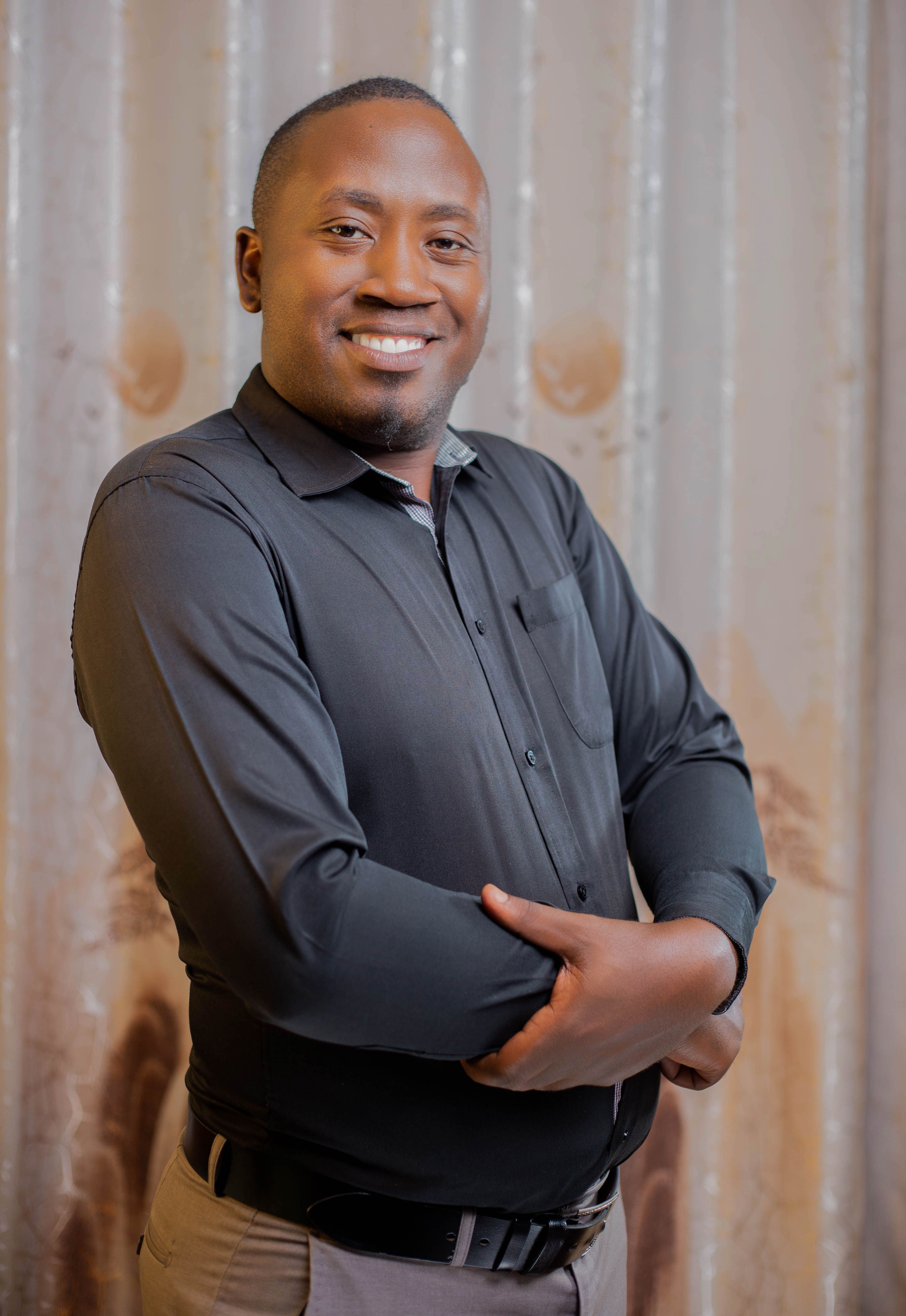 A confident man smiling warmly while posing indoors against a neutral background.