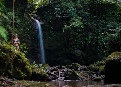 Free Woman in bikini by a serene jungle waterfall, surrounded by lush greenery and rocky terrain. Stock Photo