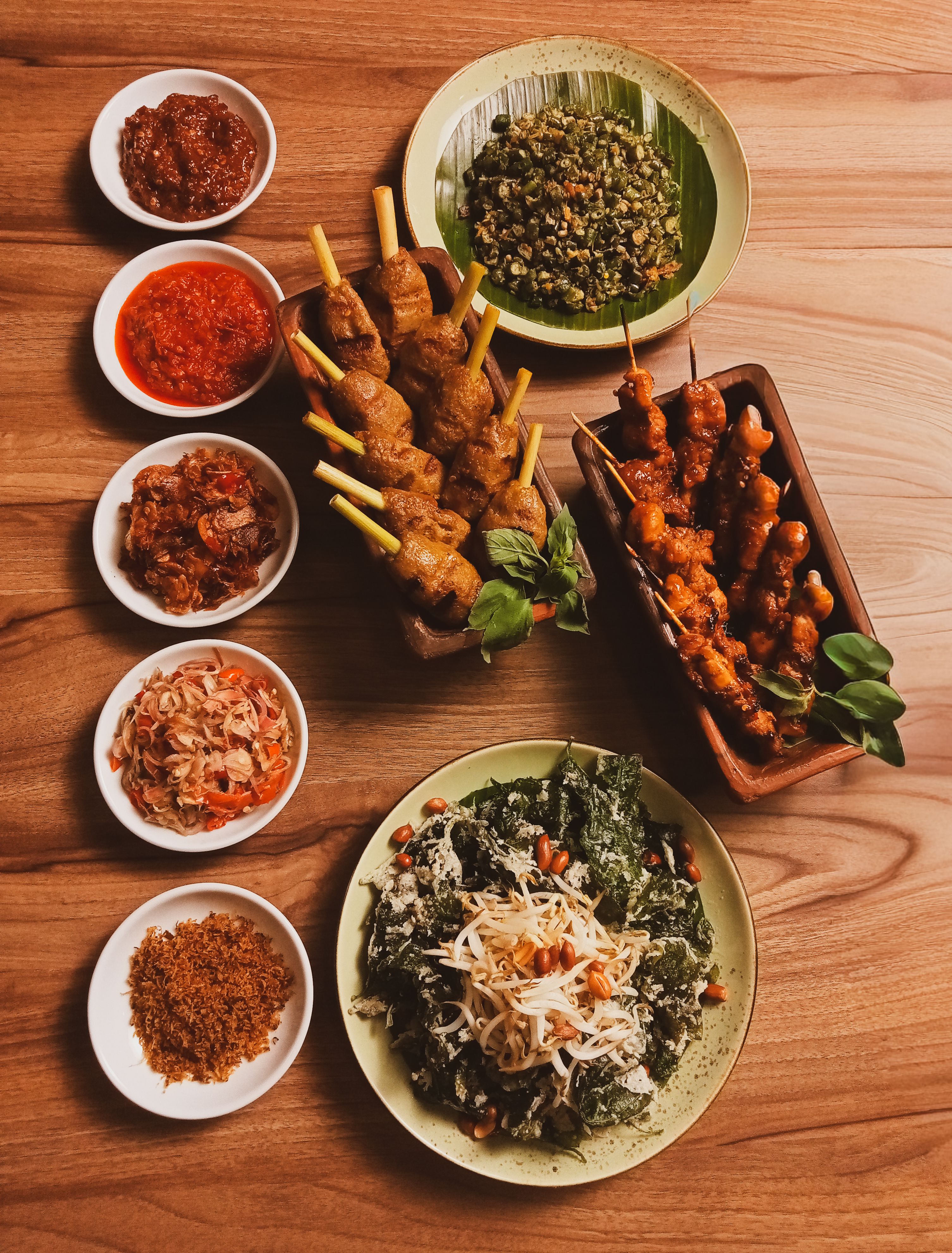 A delectable spread of Indonesian satay, sambal, and salads on a wooden table.