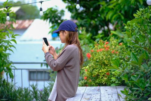 Free A woman in a garden captures the vibrant surroundings on her phone, showcasing her love for nature photography. Stock Photo