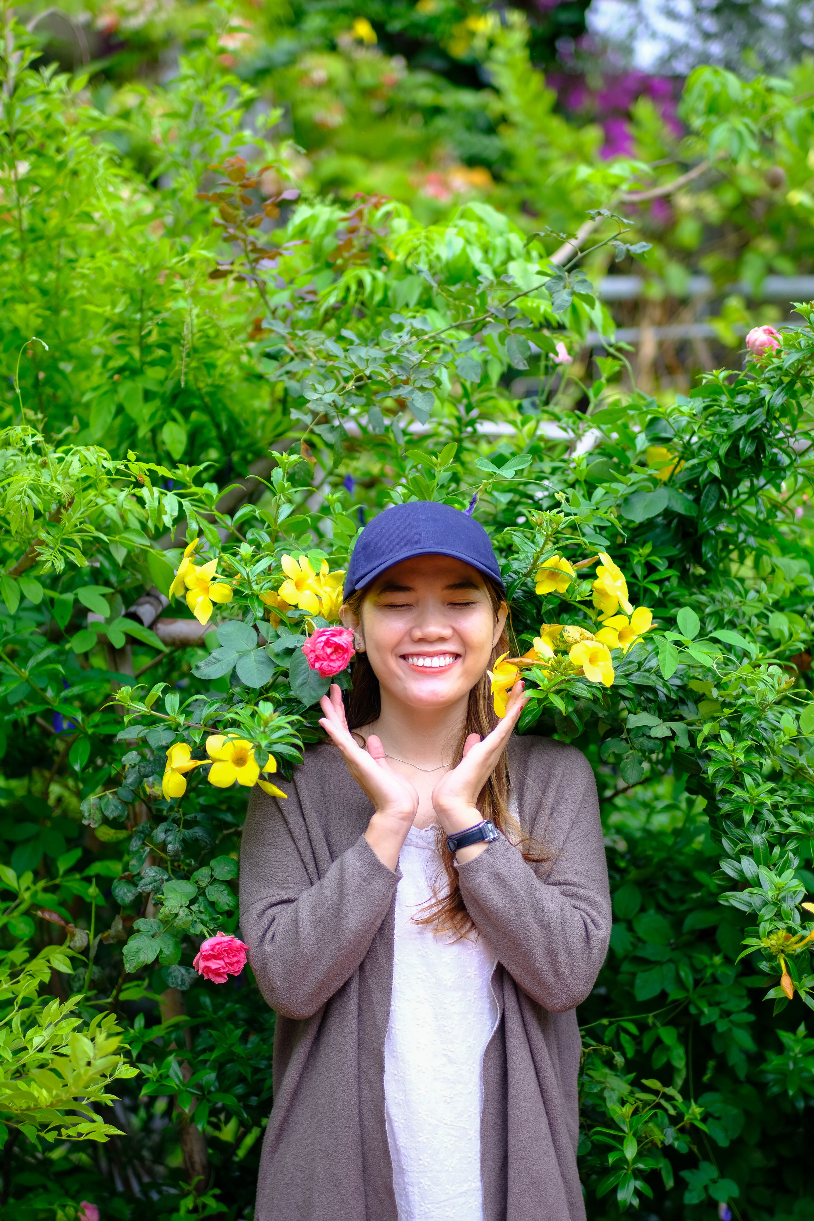Joyful young woman posing with vibrant flowers in a lush garden in Da Nang, Vietnam.