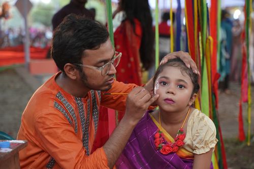 Free An adult painting a child's face at an outdoor cultural festival, surrounded by vibrant decorations. Stock Photo