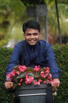 Young man in blue jacket posing with vibrant pink flowers in a garden setting. - Fotografer Sidoarjo