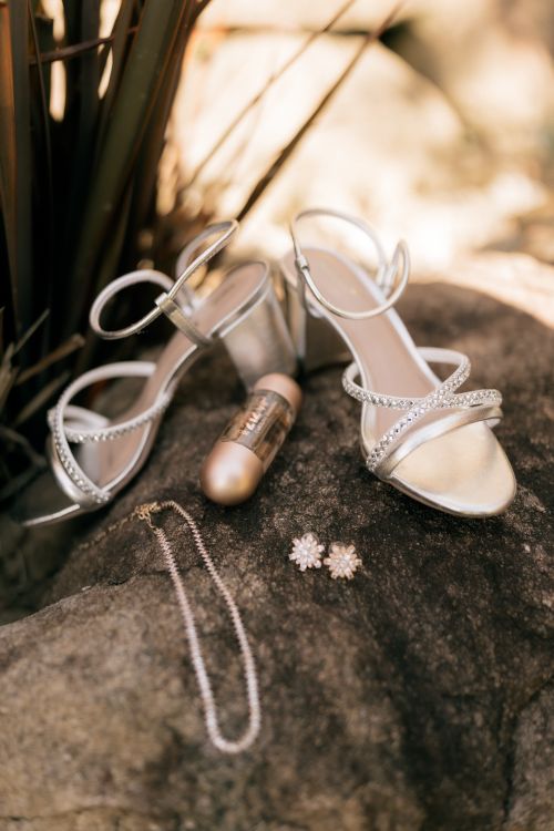 Free Elegant bridal shoes, jewelry, and lipstick elegantly displayed on a rustic rock surface outdoors. Stock Photo