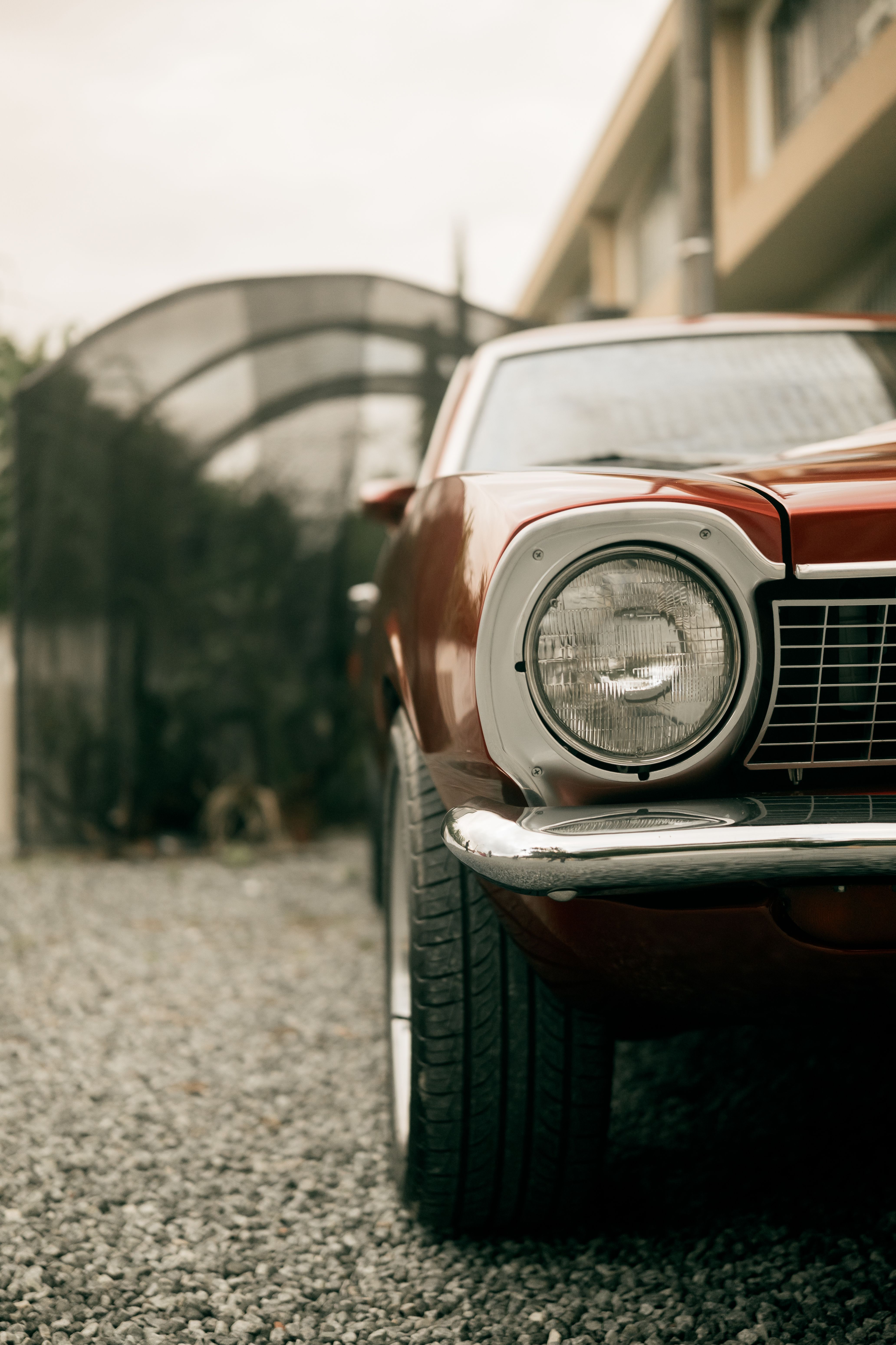 Close-up of a classic red car parked on a gravel driveway, showcasing a retro style.