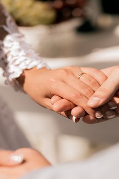 Intimate close-up of bride and groom holding hands, showcasing wedding rings during a ceremony.