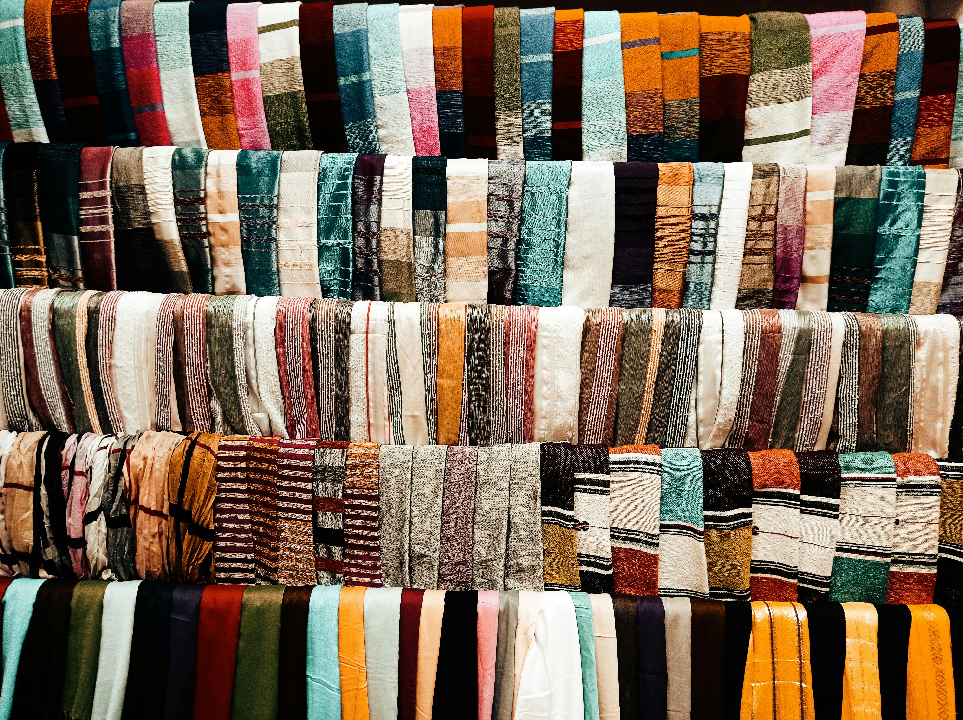 A vibrant array of multicolored fabrics neatly arranged in a market stall, showcasing diverse patterns and textures. — Maynard Longarm Quilting