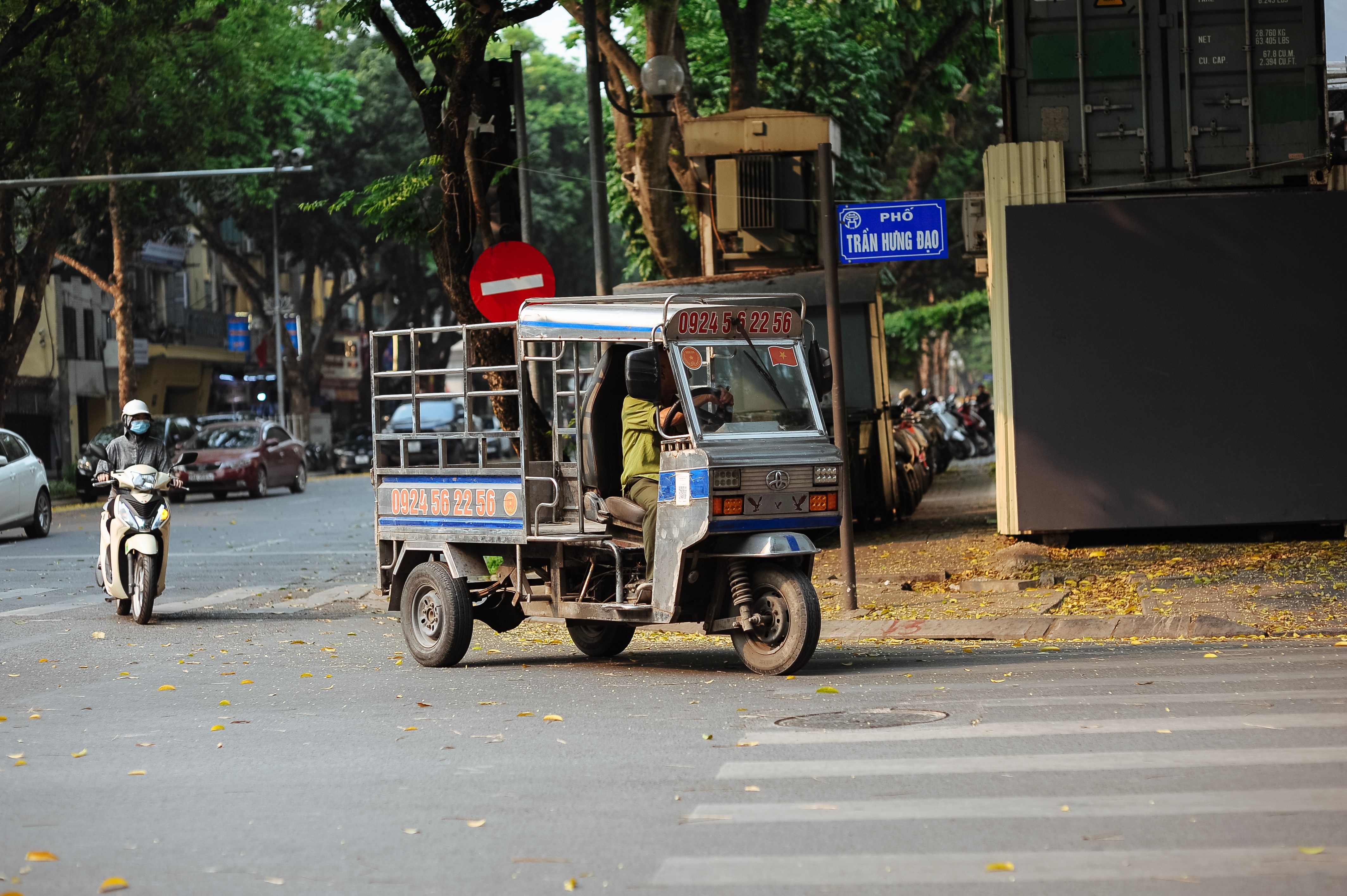 A bustling street in Hanoi with a motorcycle and tricycle on a sunny day.