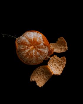 A dramatic close-up of a partially peeled orange against a dark background, showcasing texture and contrast.