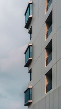 A modern high-rise building featuring distinct geometric balconies against a pastel sky.